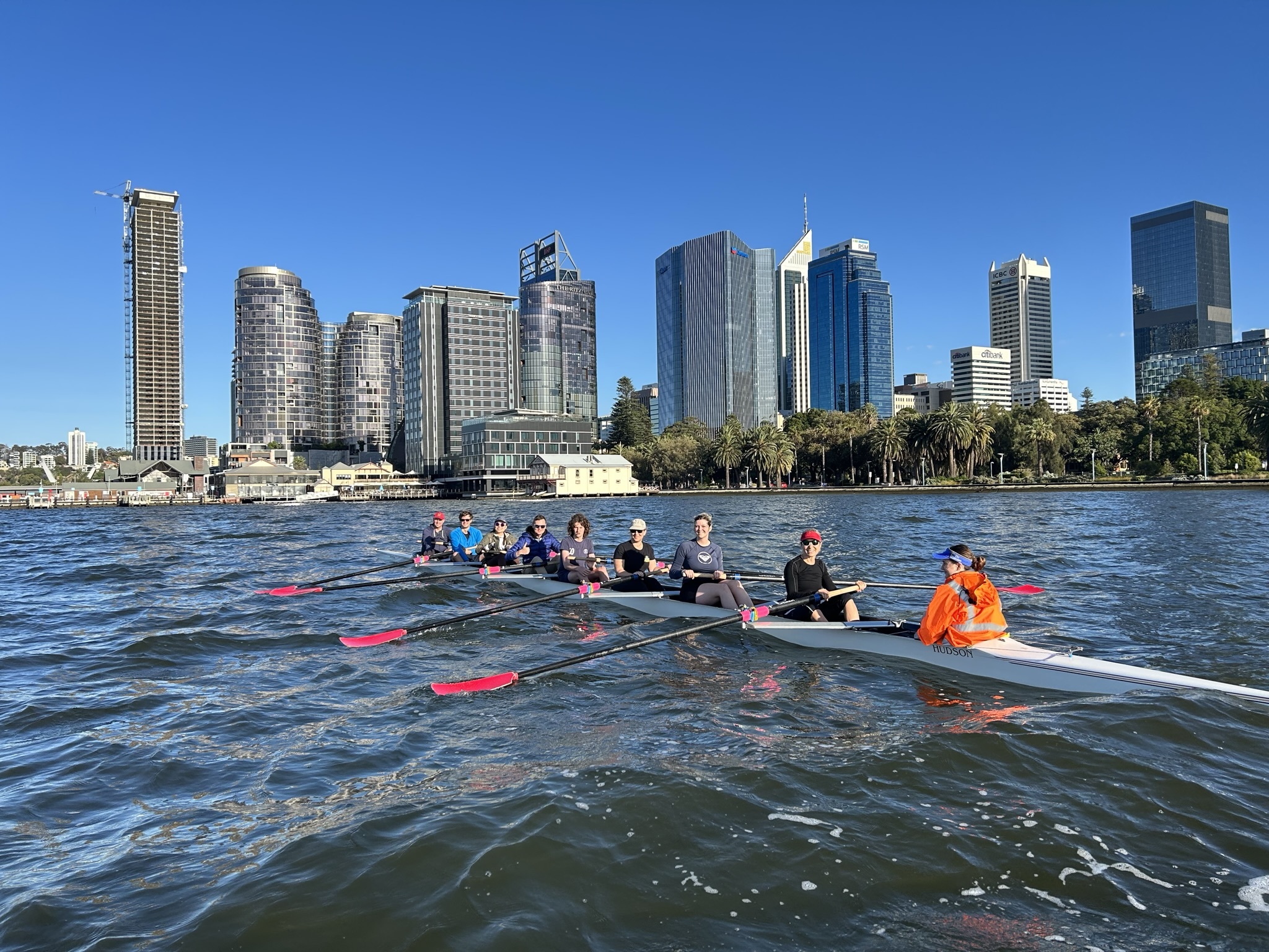 9 people in a row boat on the Swan River, Perth city in the background.